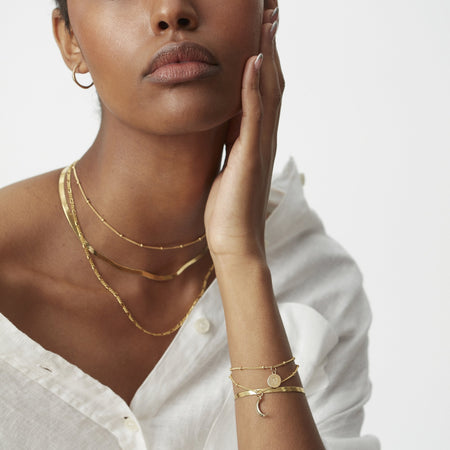 model in white shirt wearing a gold bead chain choker necklace, a flat snake chain necklace in gold and a gold figaro chain necklace